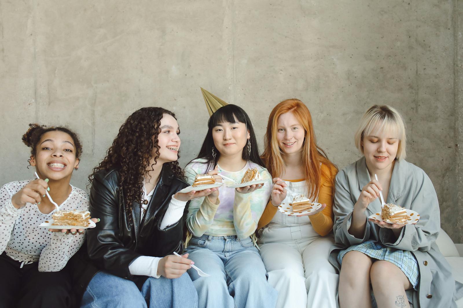 Five young women celebrating with cake indoors, showcasing diversity and friendship.